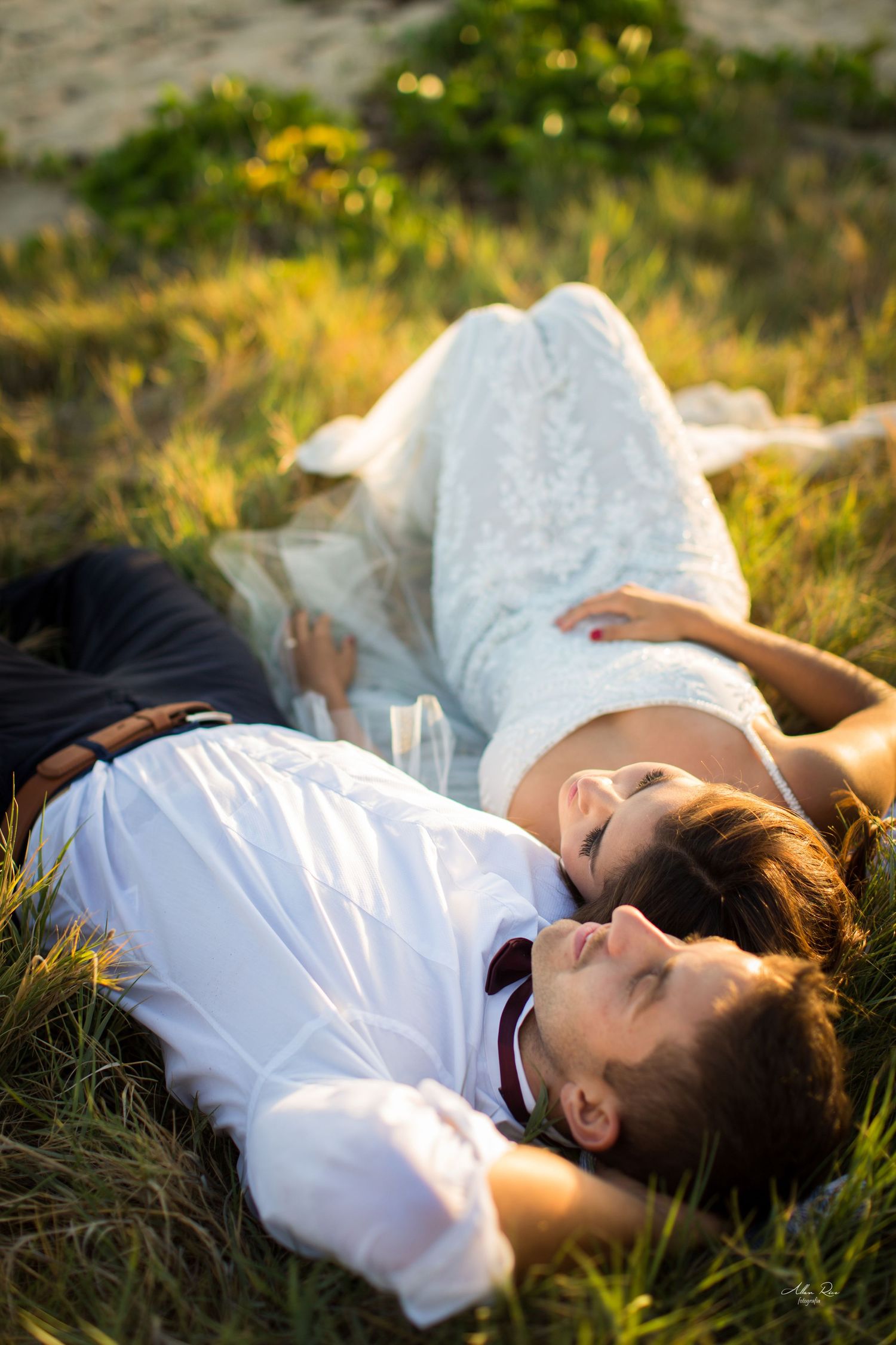 Bride and groom lie peacefully in lush green grass, gazing upward in warm golden afternoon sunlight.