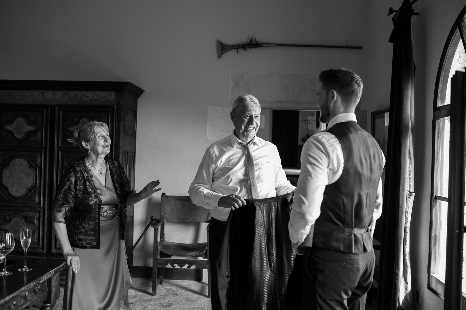 Groom chatting with parents in a vintage room before the wedding ceremony in black and white.