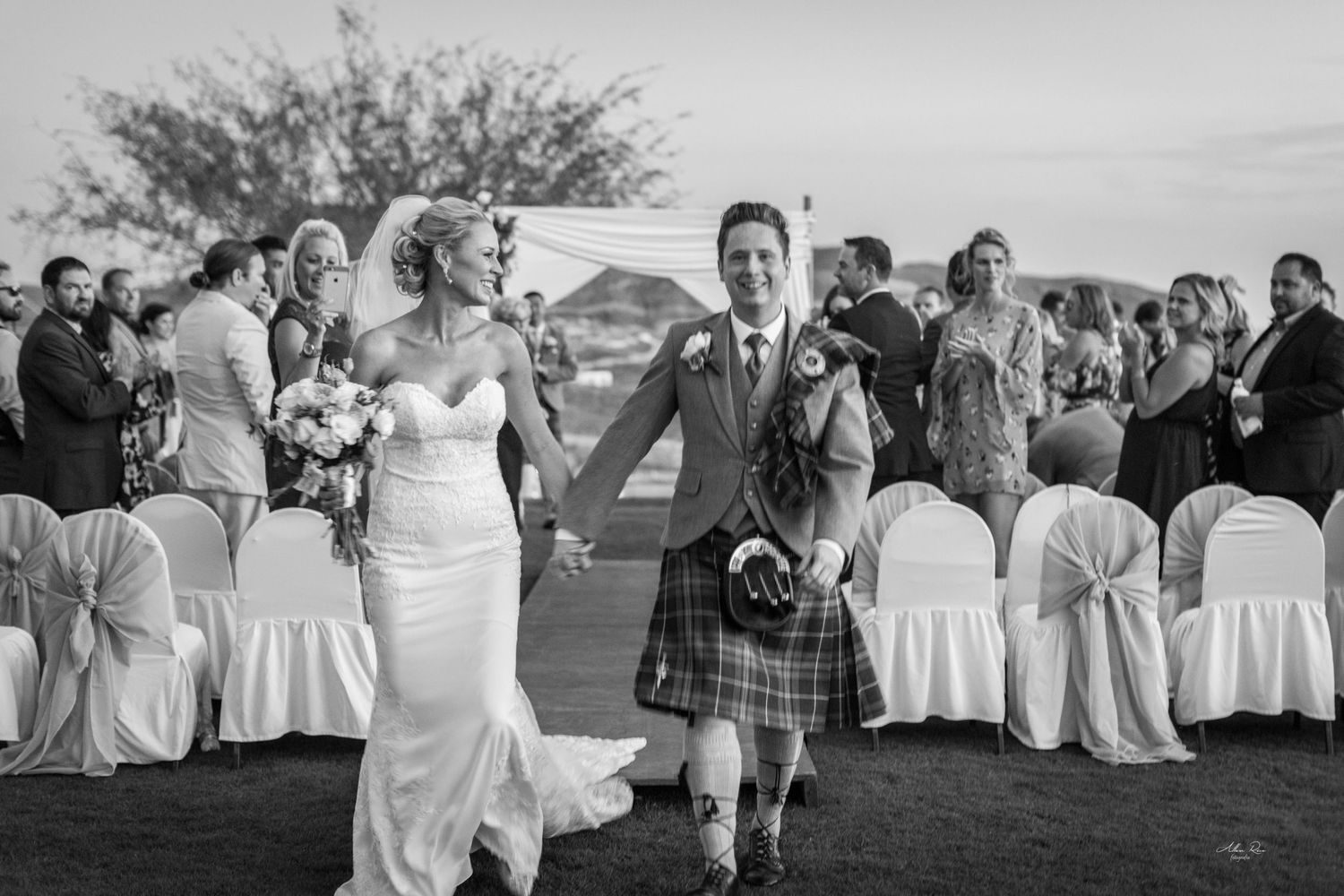 Bride and groom walking joyfully down the aisle after their outdoor wedding ceremony with guests applauding.