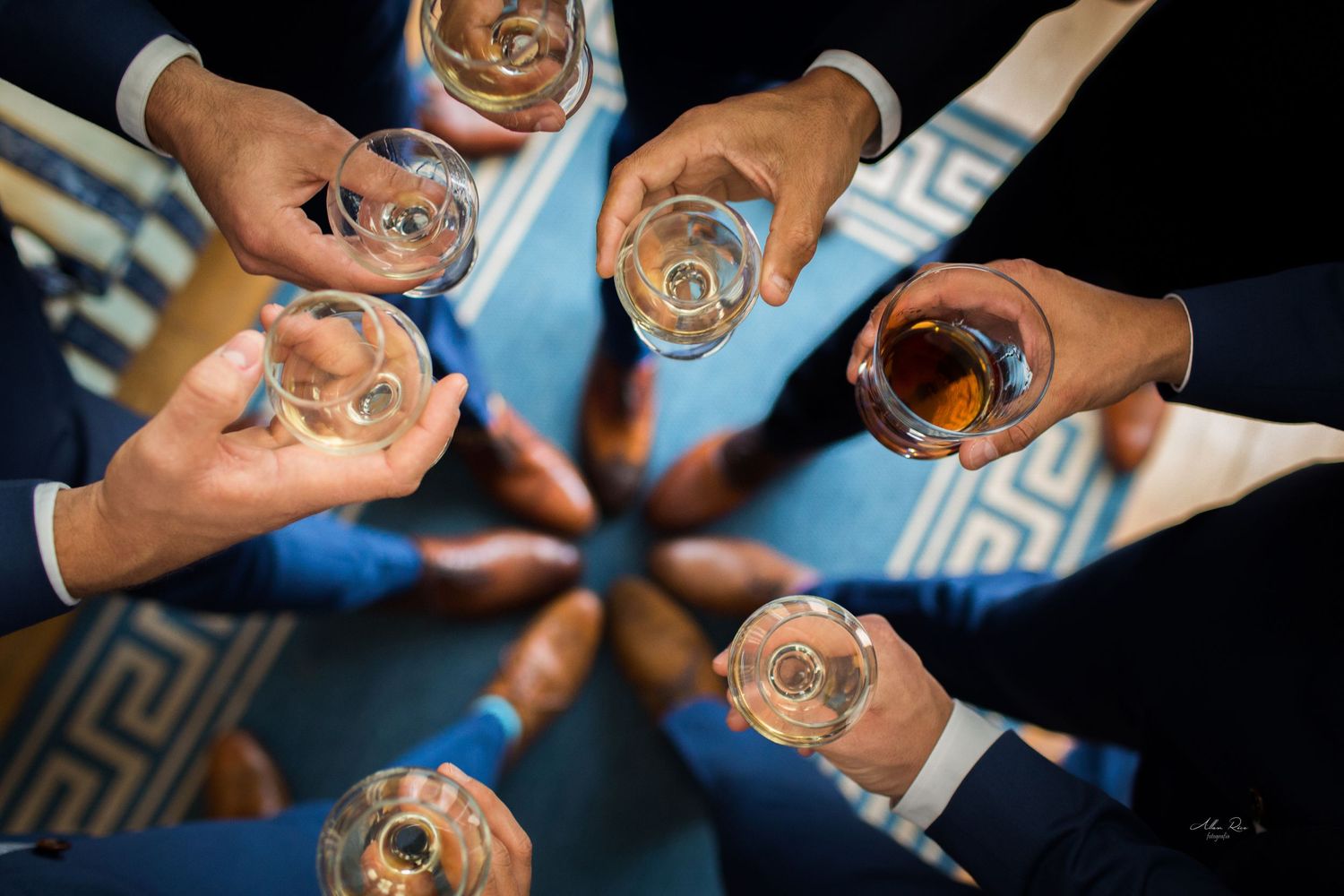 Overhead view of groomsmen in blue suits toasting with glasses of whiskey in a circle.
