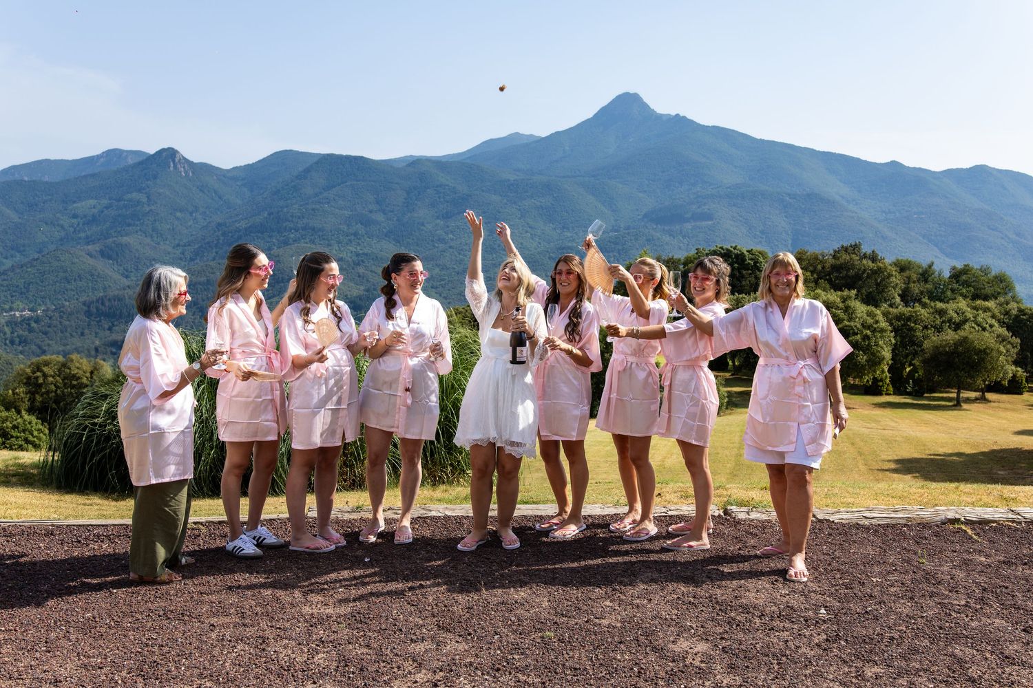 Bridal party in matching pink robes celebrating outdoors with mountains in the background.