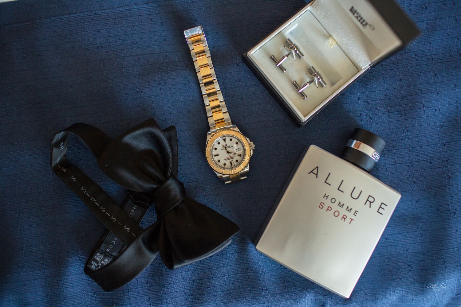 Groom accessories flatlay with gold watch, bow tie, cufflinks, and Chanel Allure cologne.