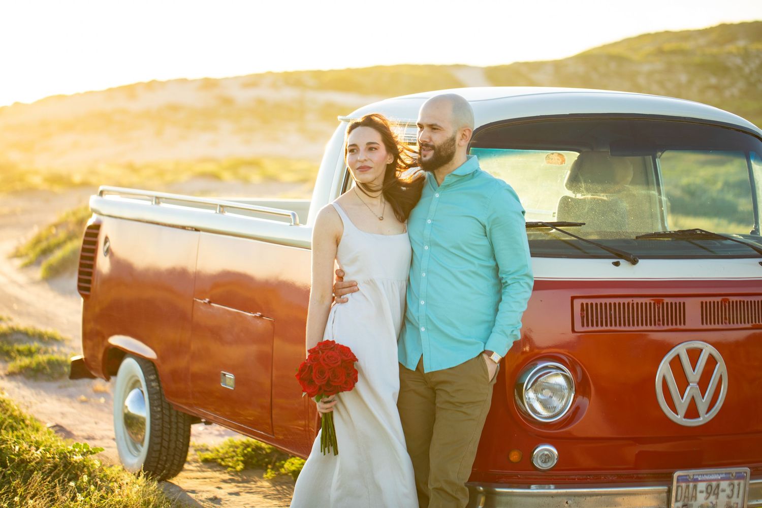 Bride and groom posing beside a vintage red VW bus at golden hour.