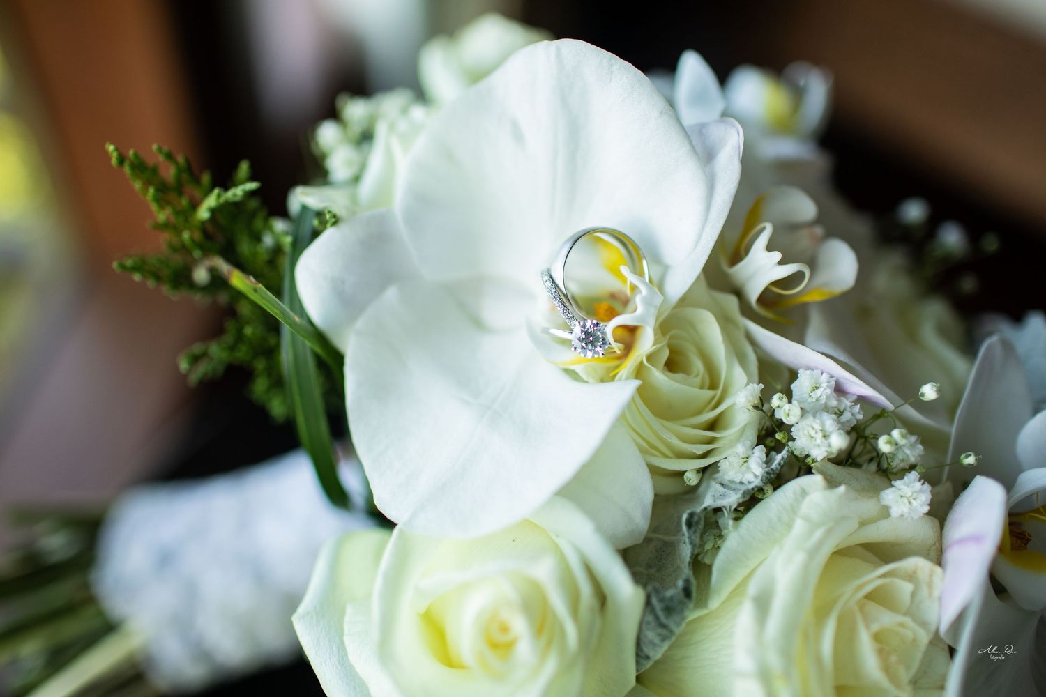 Wedding rings nestled among white orchids and roses in bridal bouquet.