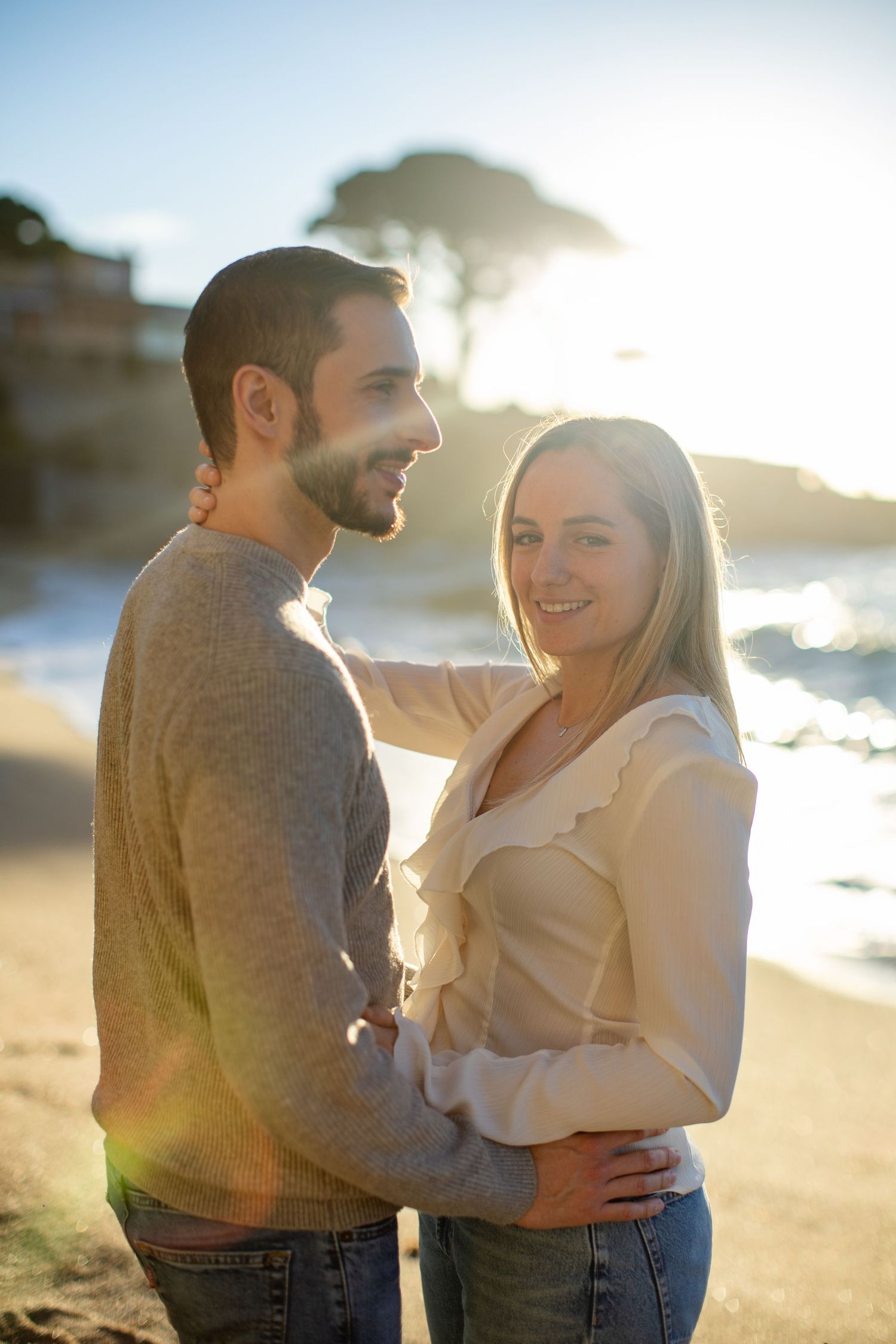 Couple embracing on a golden sunlit beach with ocean waves in the background.