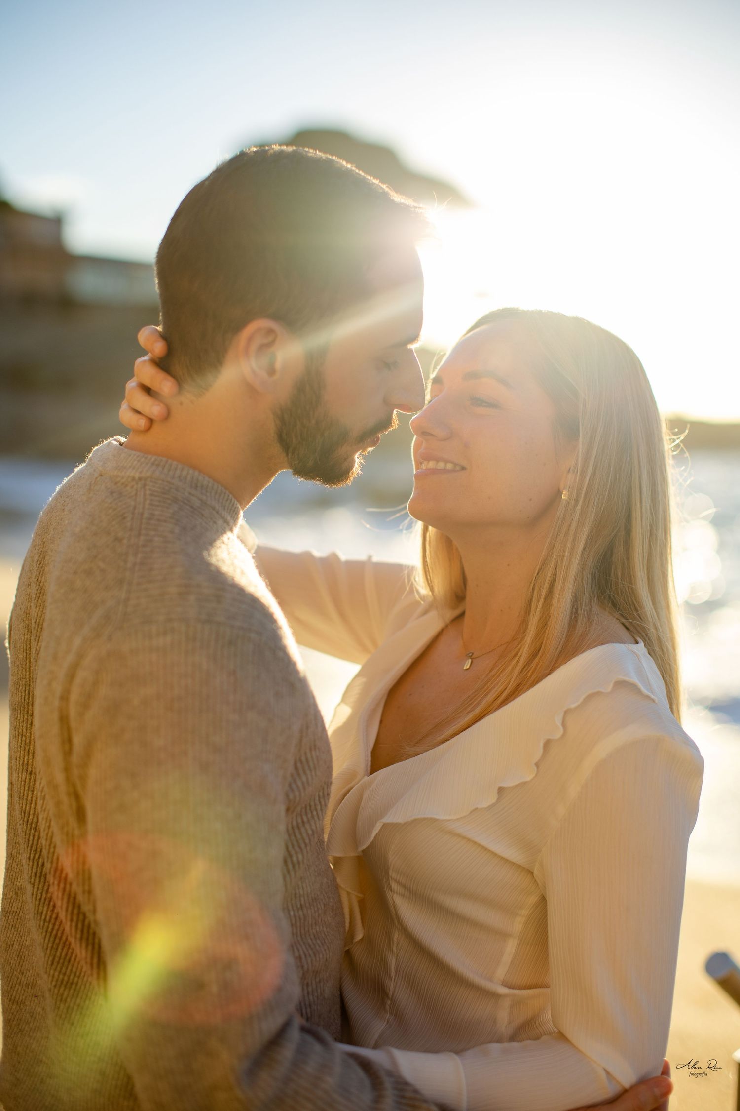 Romantic couple almost kissing on a beach with golden sun flare glowing behind them.