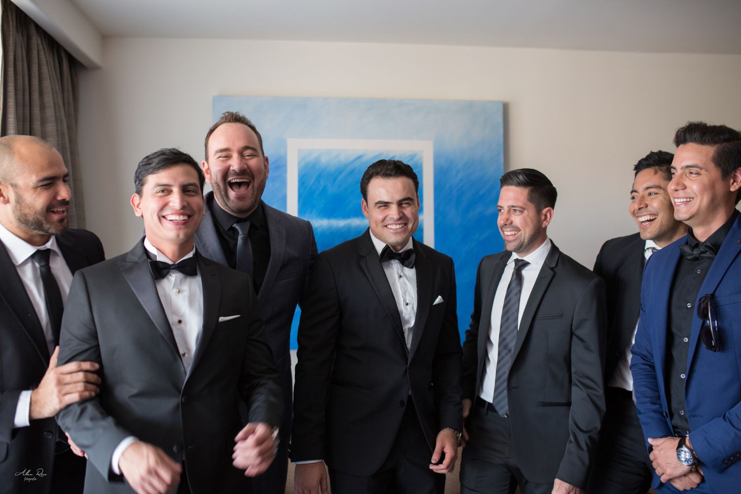 Joyful groom and groomsmen laughing together in tuxedos before wedding ceremony.