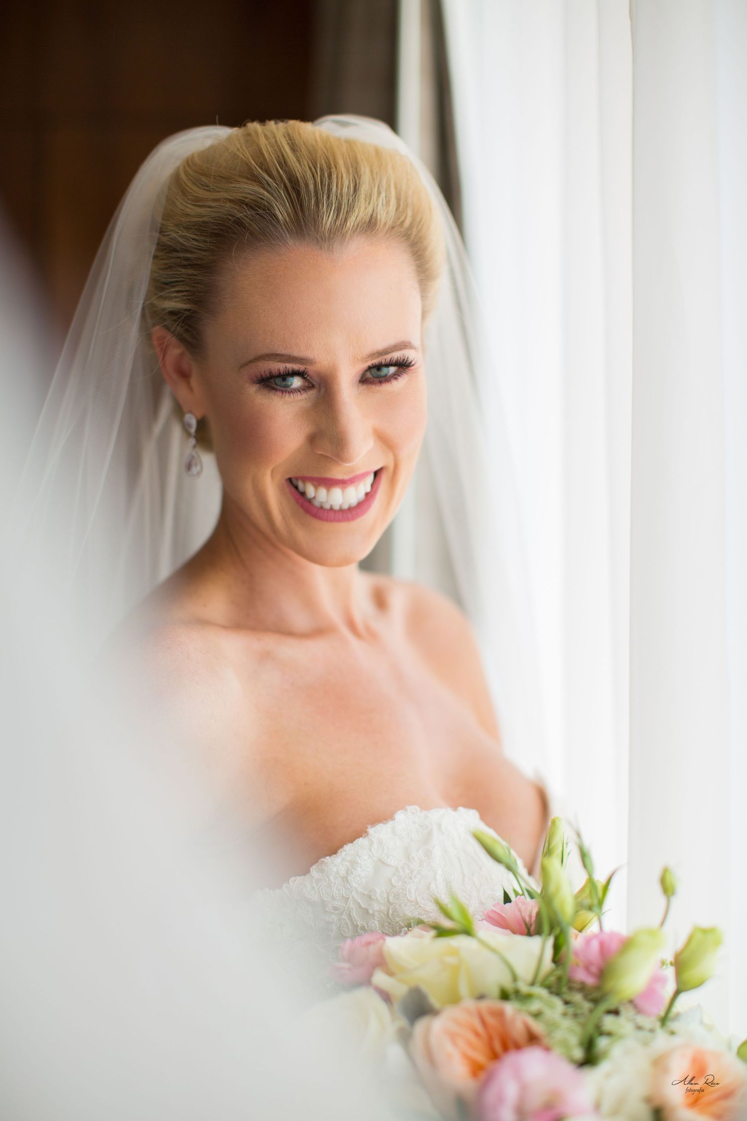 Smiling bride in a white wedding dress with veil holding a pink and white floral bouquet.