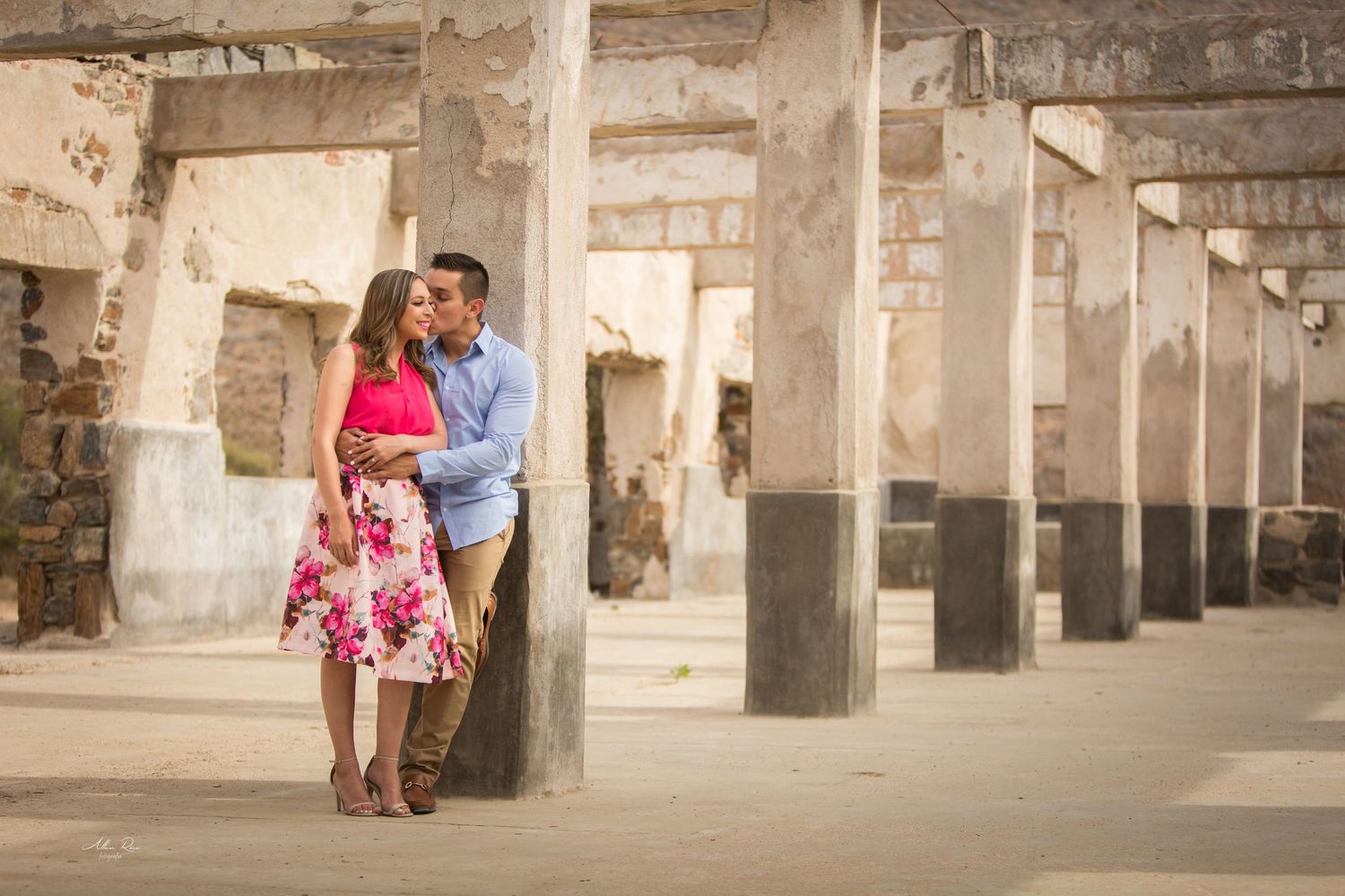 Couple sharing a tender kiss leaning against a column in a rustic outdoor ruins engagement session.