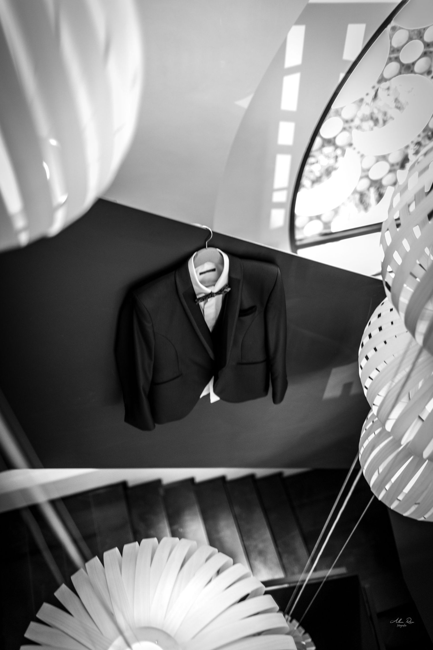 Black and white photo of a groom's suit hanging on a staircase railing.