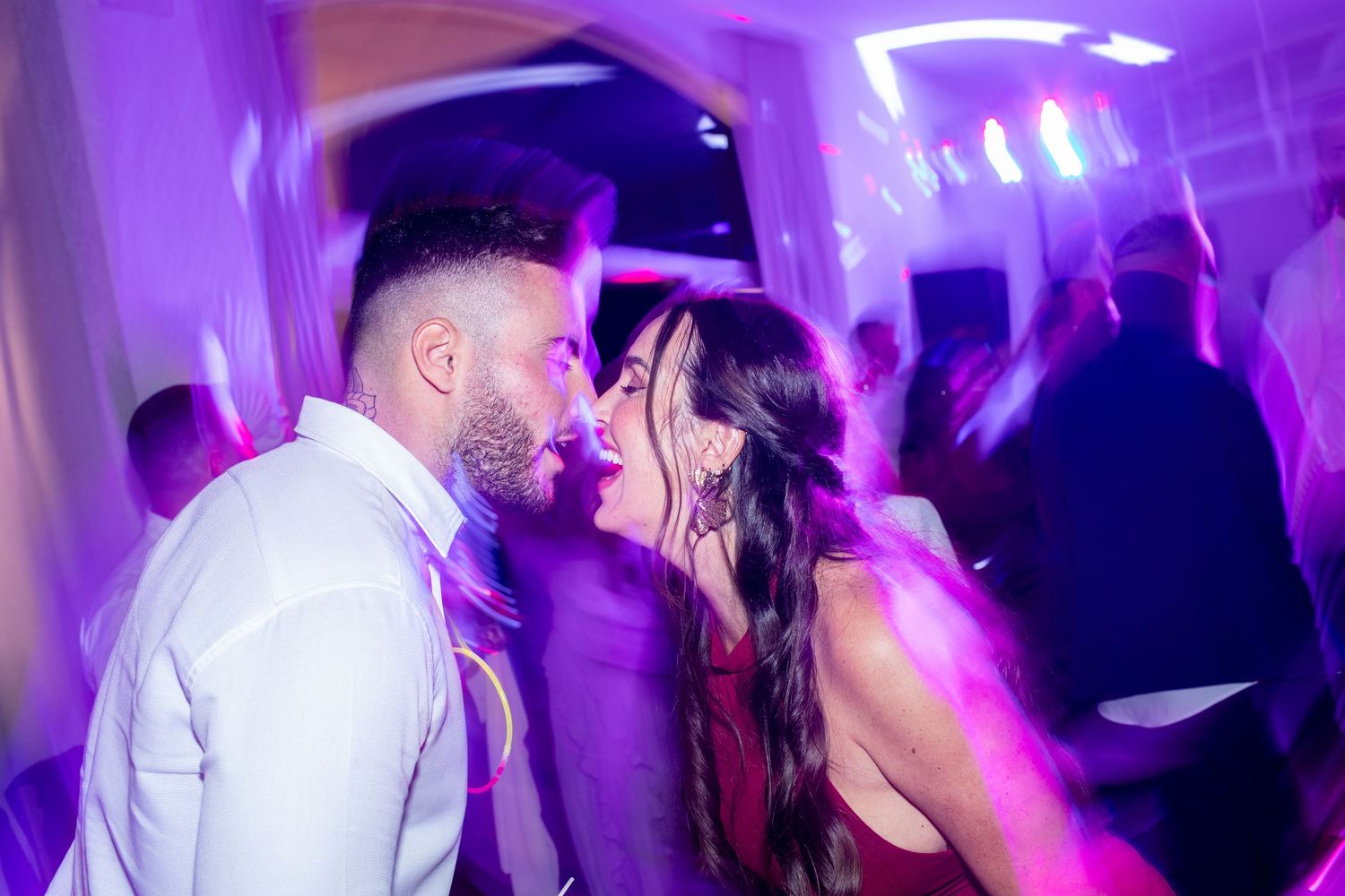Couple sharing a romantic moment on the dance floor under purple lights at a wedding reception.