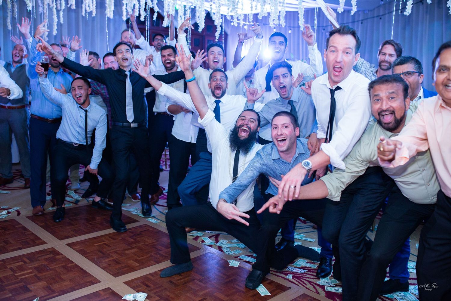 Large group of men posing and celebrating together on a dance floor at a wedding reception.