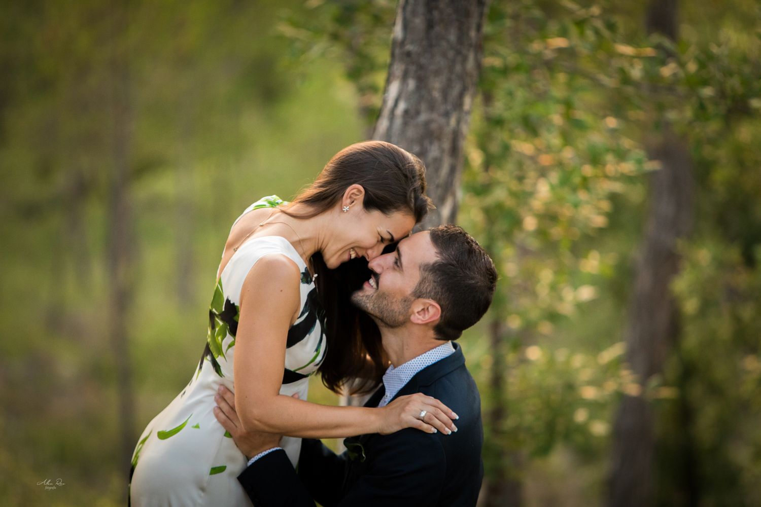 Groom lifting bride for a playful kiss in a lush green forest setting.