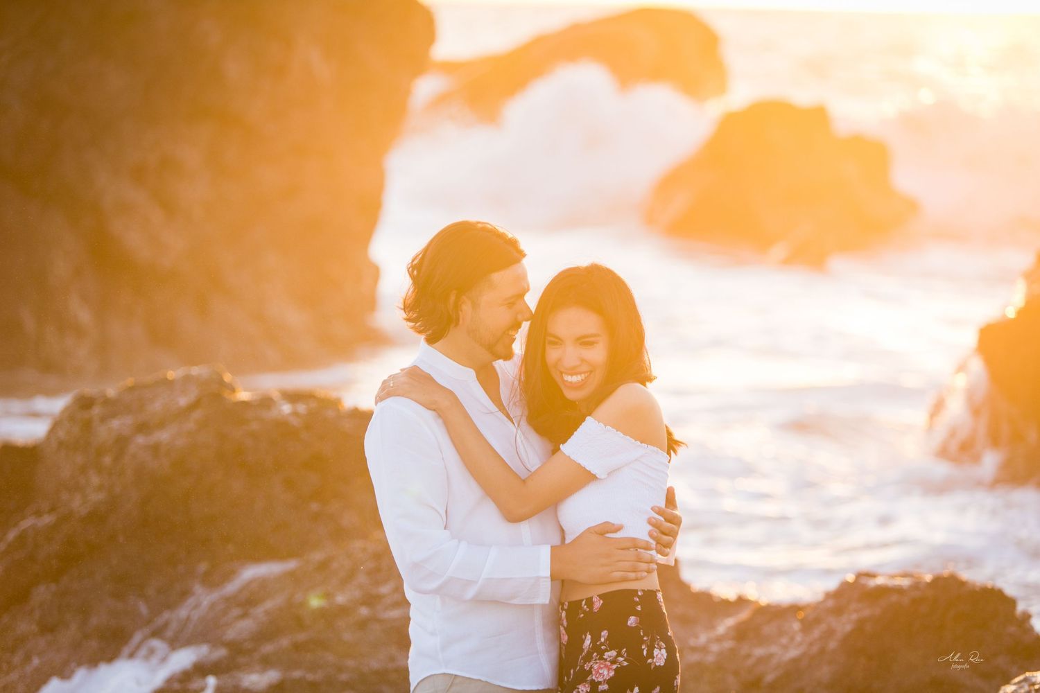 Romantic couple embracing at golden sunset on rocky ocean shore.