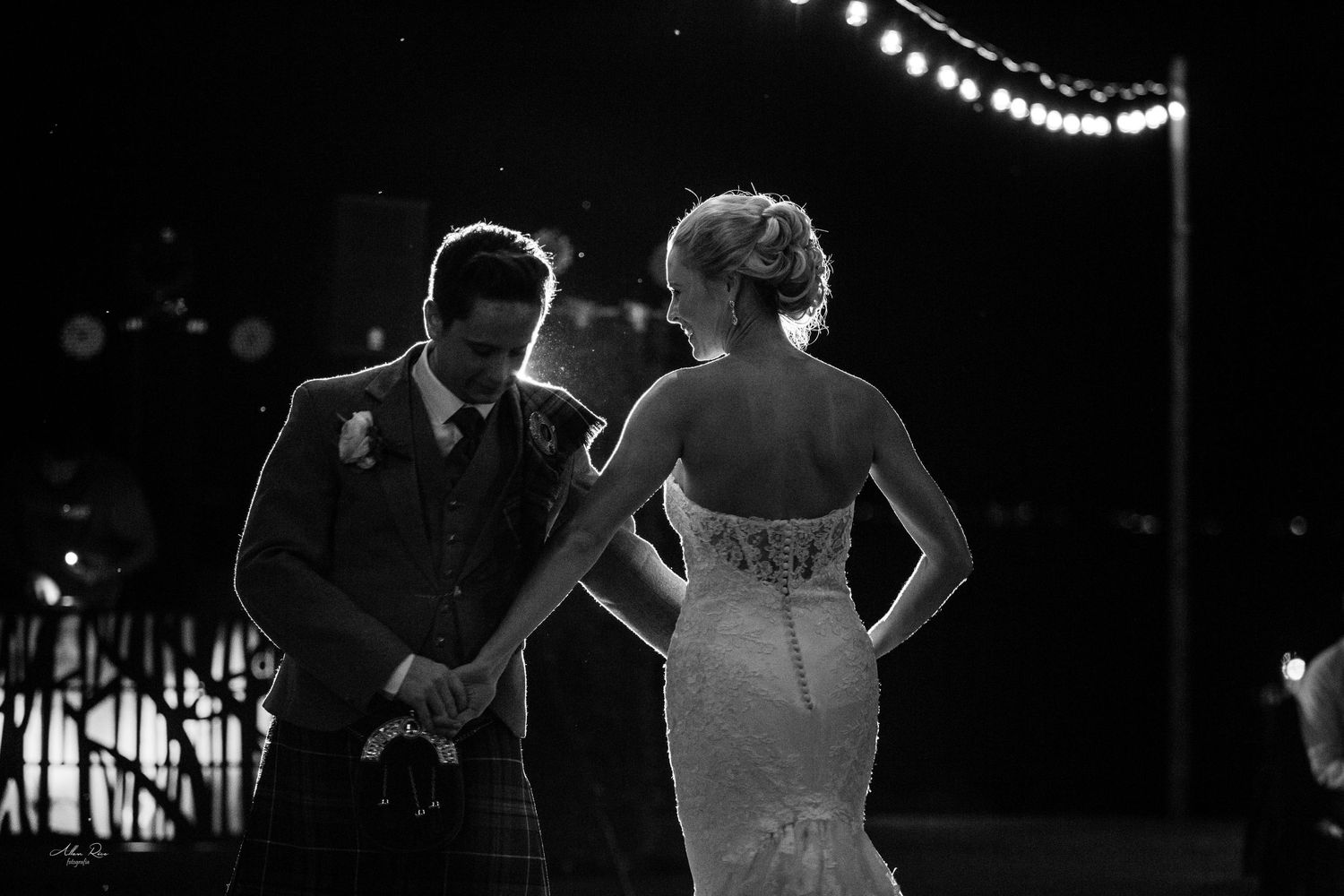 Bride and groom holding hands walking away in a romantic black and white night wedding reception photo.