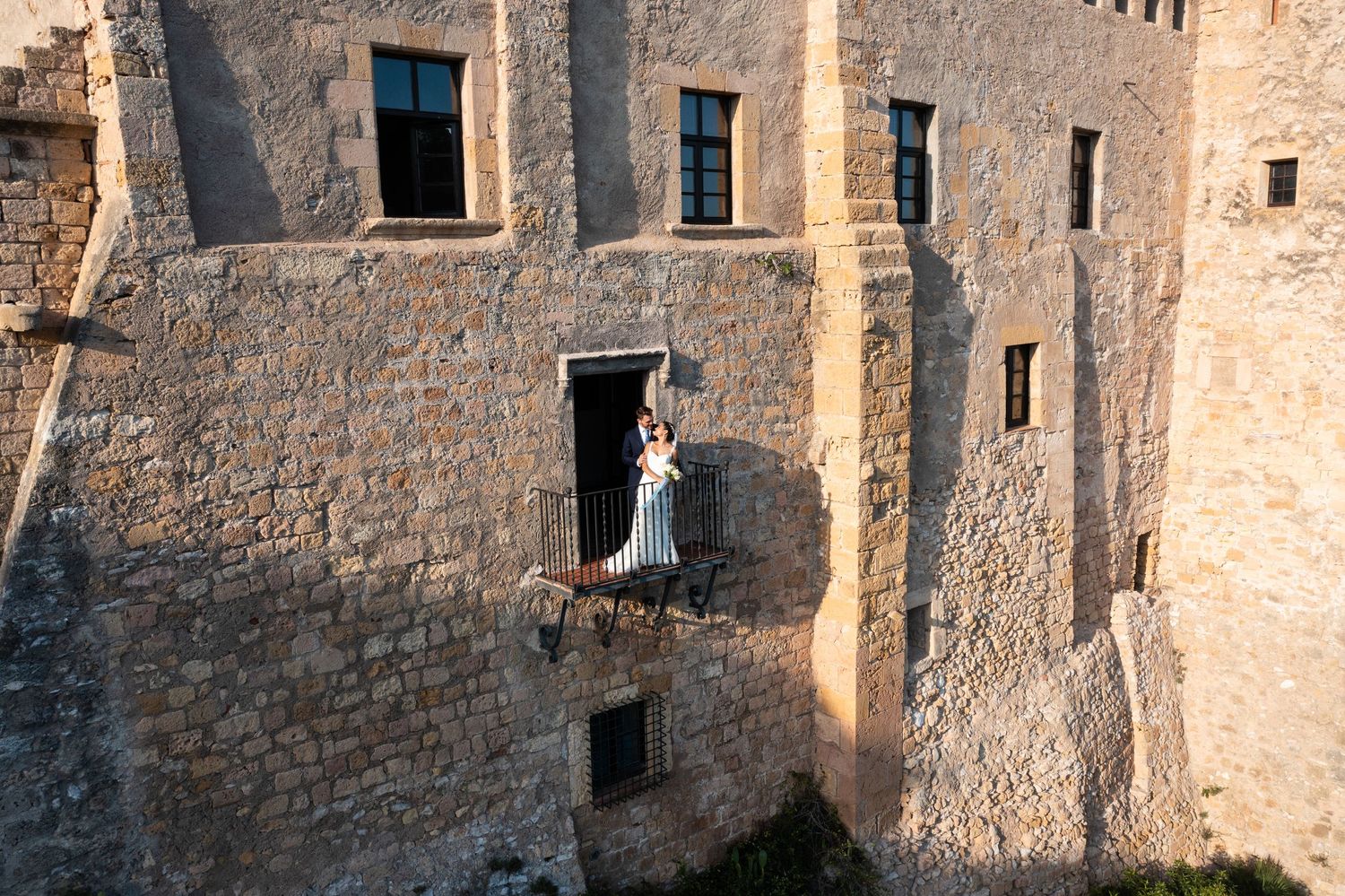 Bride in white gown stands in a dramatic stone castle doorway bathed in warm golden sunlight.