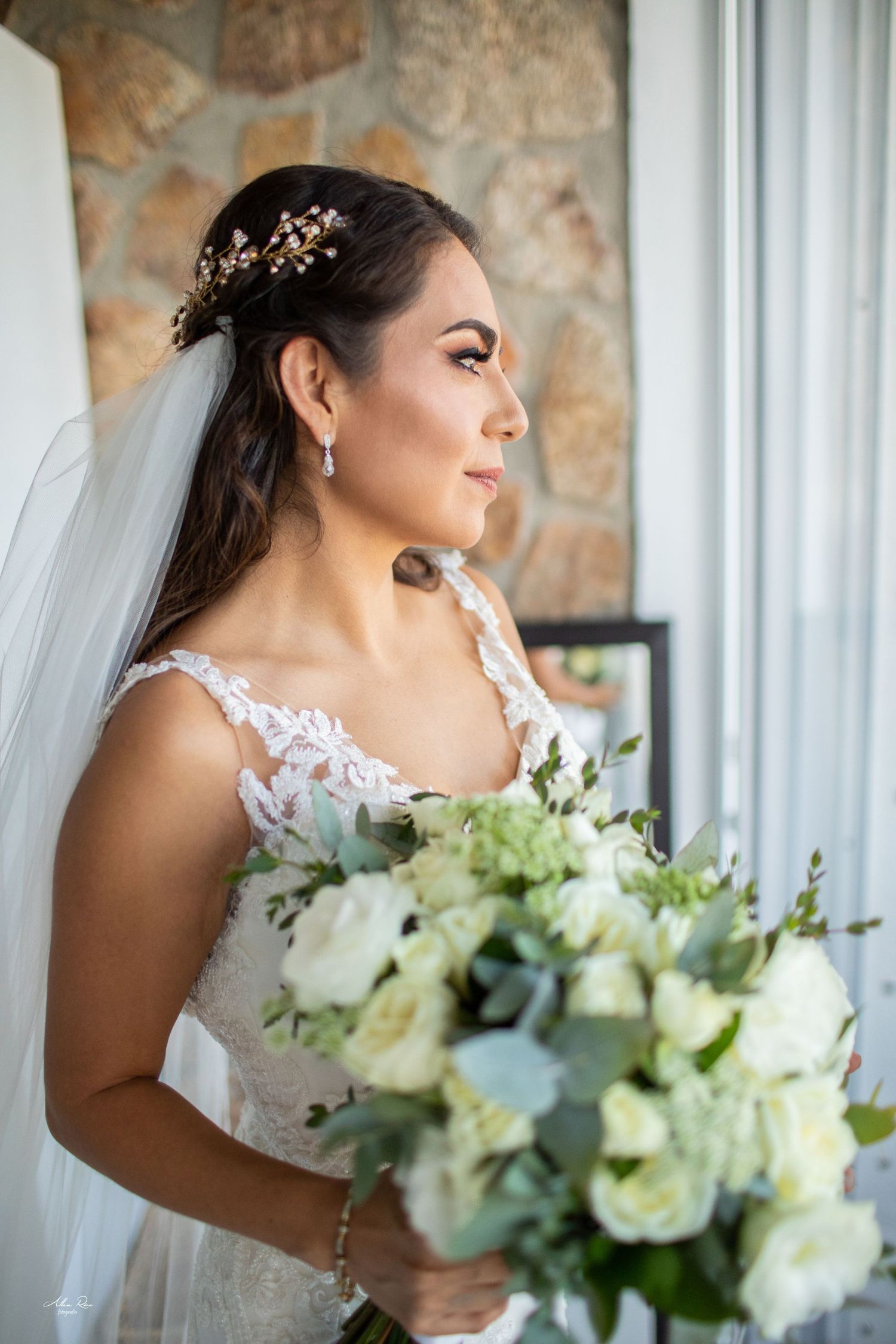 Beautiful bride in lace gown holding white rose bouquet with gold hair accessory and veil.