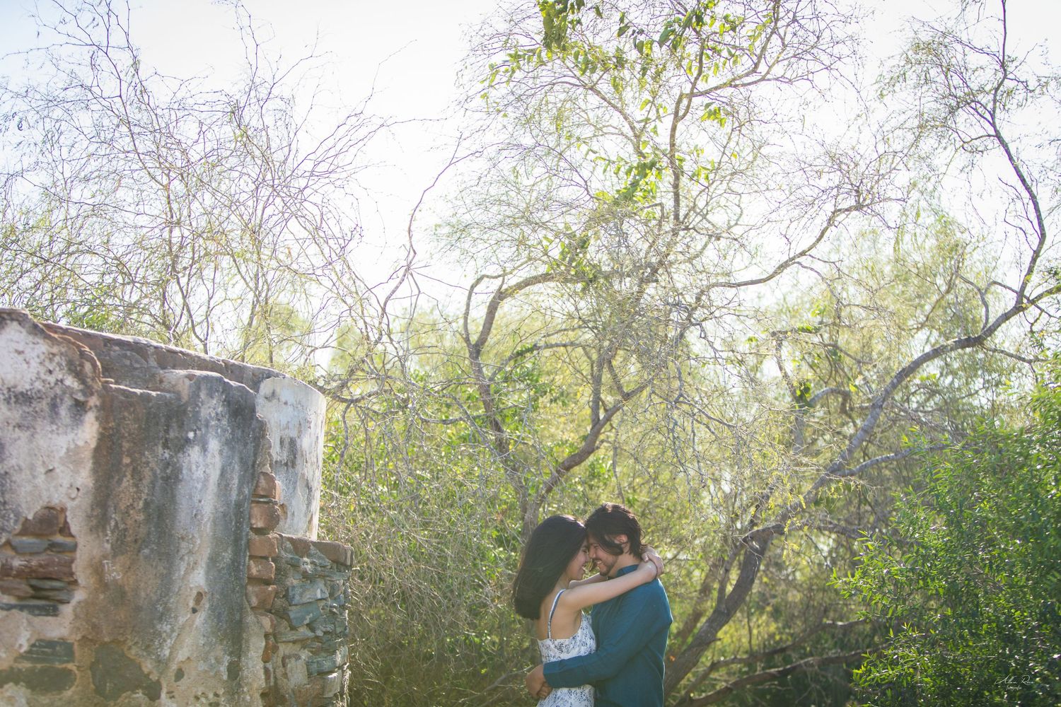 Romantic couple embraces tenderly among rustic ruins and lush greenery in an outdoor engagement session.