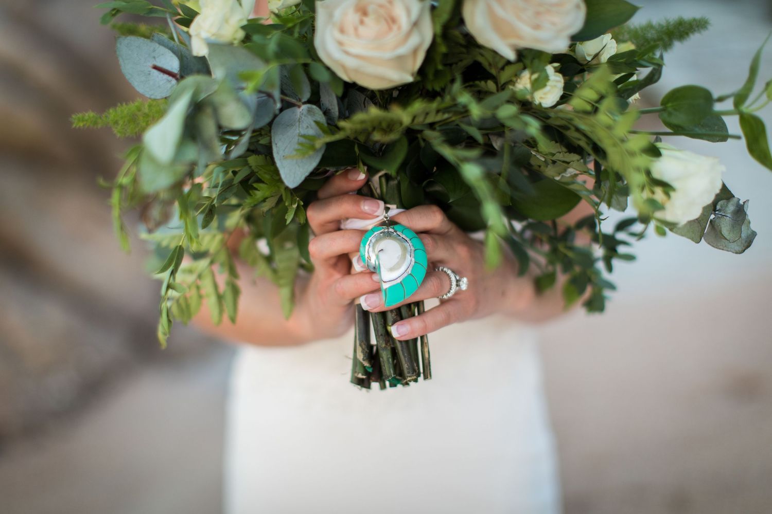 Close-up of bridal bouquet with white roses, greenery, and a turquoise charm detail.