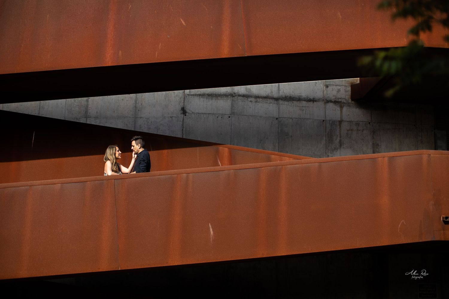 Couple sharing a romantic moment on a rustic metal structure at golden hour.