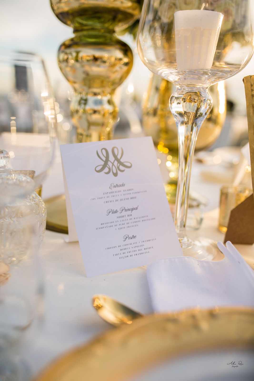 Elegant wedding reception table setting with gold accents, crystal glassware, candles, and a formal menu card.