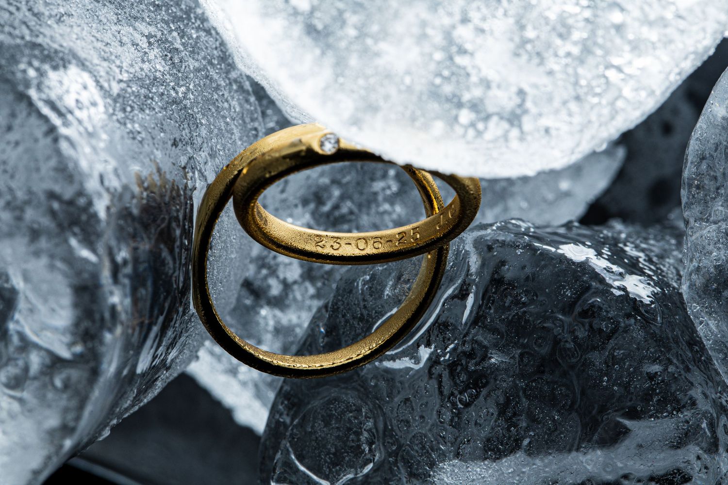 Two gold wedding bands with diamond detail elegantly displayed on clear ice cubes.