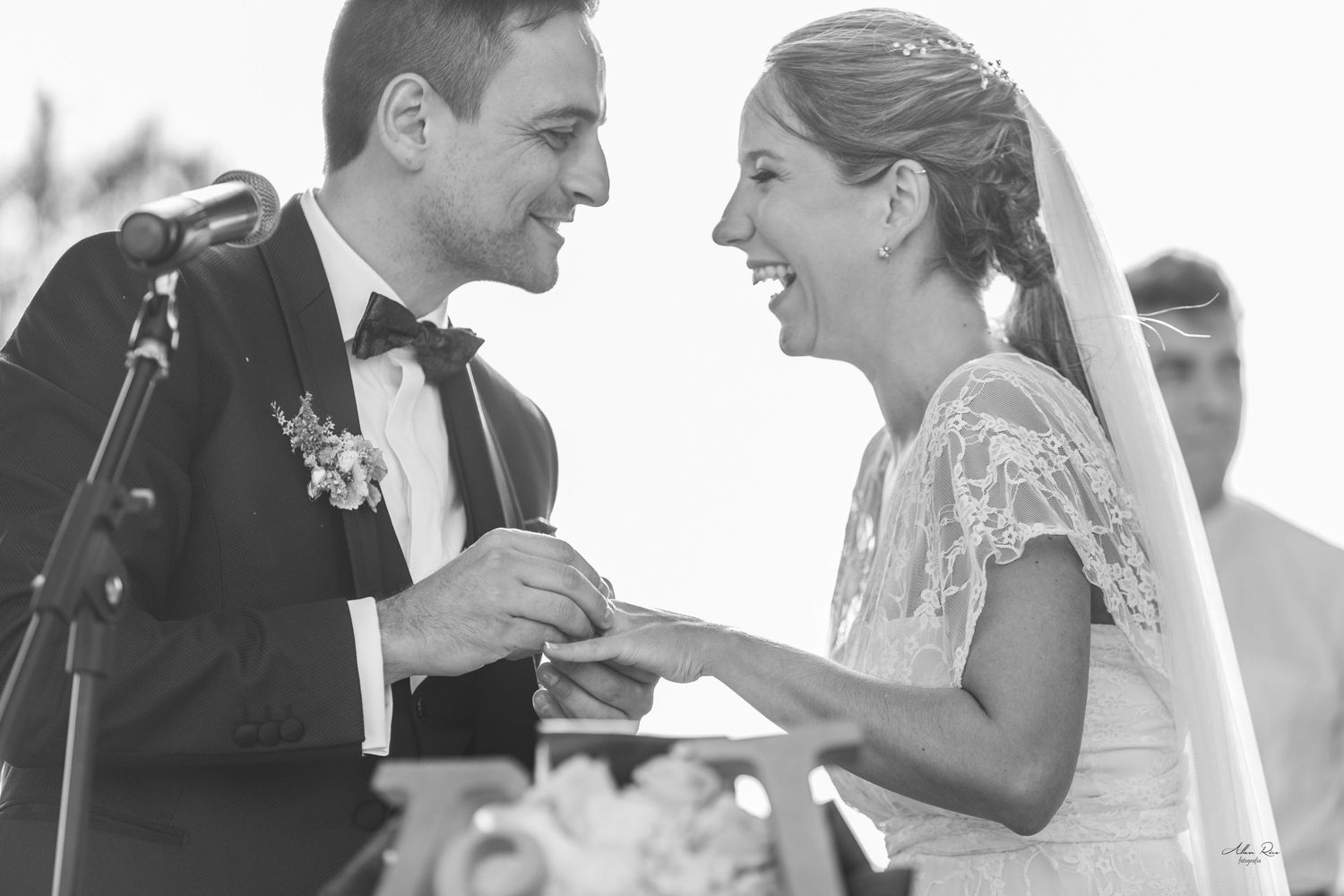 Black and white photo of groom placing ring on laughing bride at ceremony.