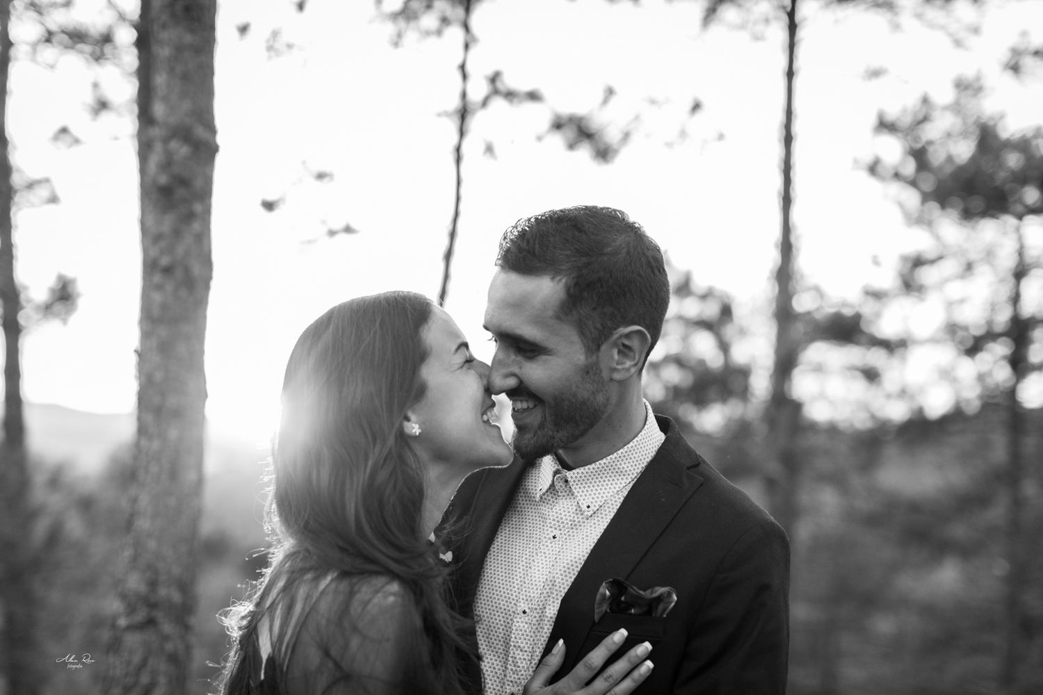 Black and white portrait of a joyful couple sharing an intimate moment in sunlit woods.