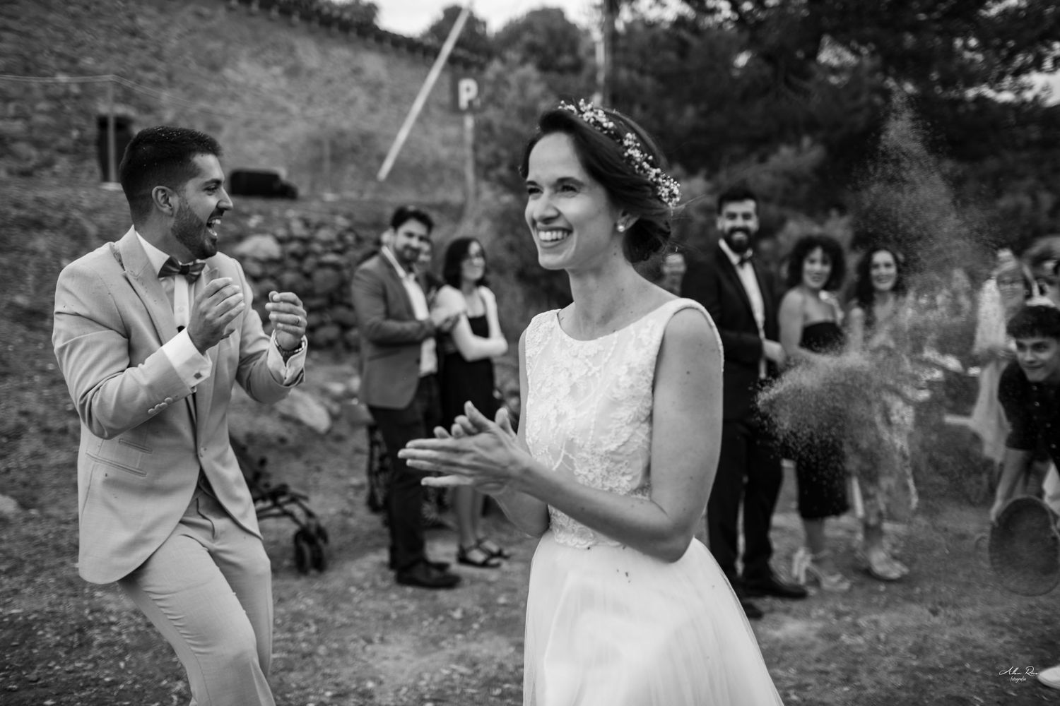 Bride laughs joyfully in black and white photo as guests celebrate at outdoor wedding.