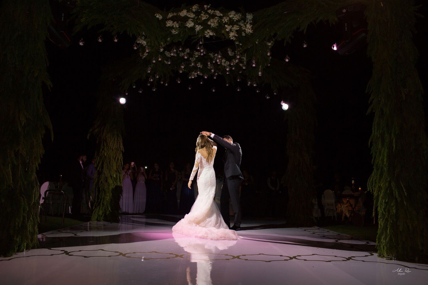 Bride and groom sharing first dance under floral arch at elegant night wedding.