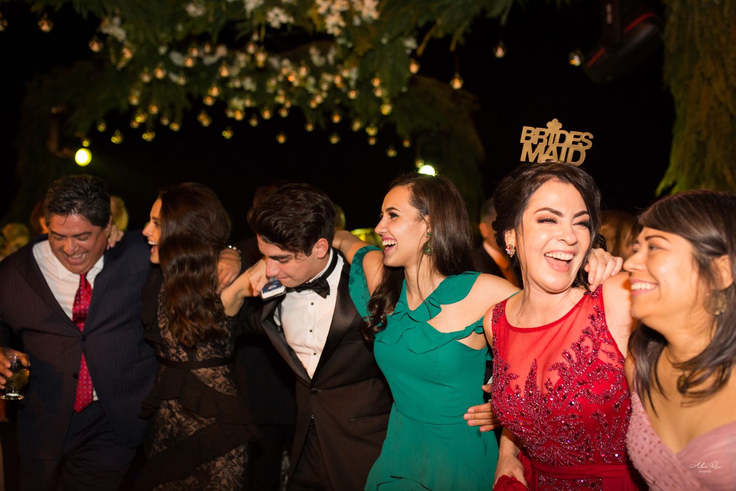Bridesmaid in red dress with tiara dances joyfully with guests at wedding celebration.