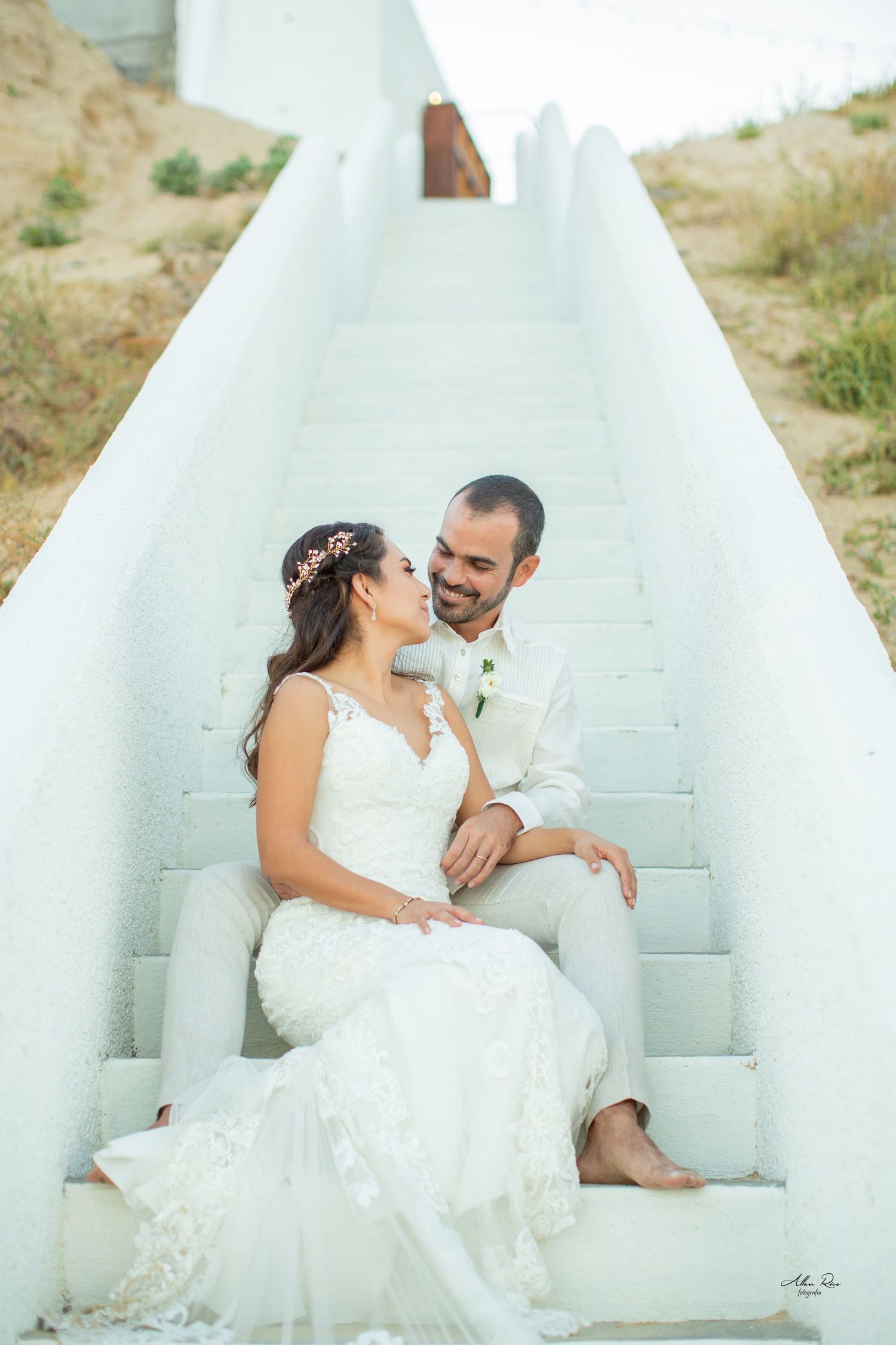 Newlywed couple sitting closely on white outdoor staircase sharing a tender romantic moment together.