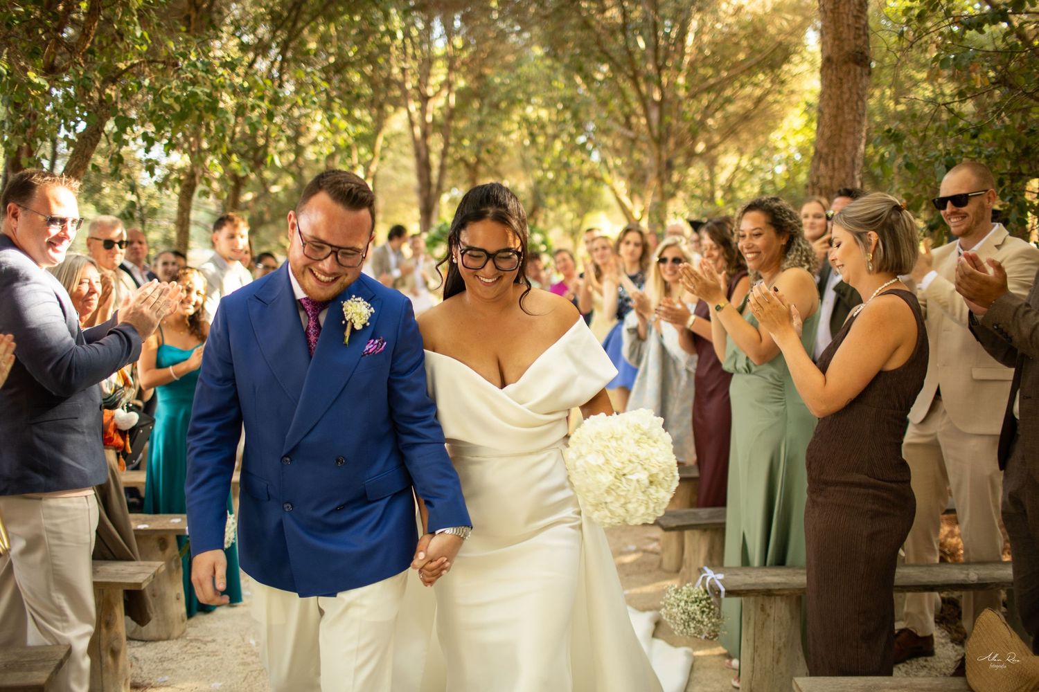 Joyful newlyweds walk down the aisle as guests celebrate at an outdoor wedding ceremony.
