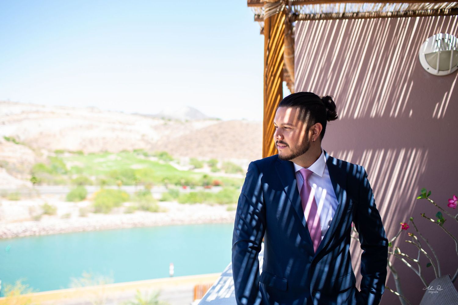 Stylish groom in a navy suit gazing at a scenic lakeside view on a sunny day.