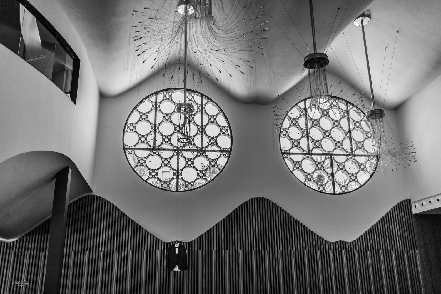 Black and white interior shot of a church with ornate round windows and chandeliers.