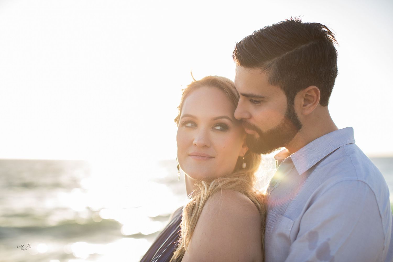 Romantic couple portrait at golden sunset by the ocean with warm lens flare.