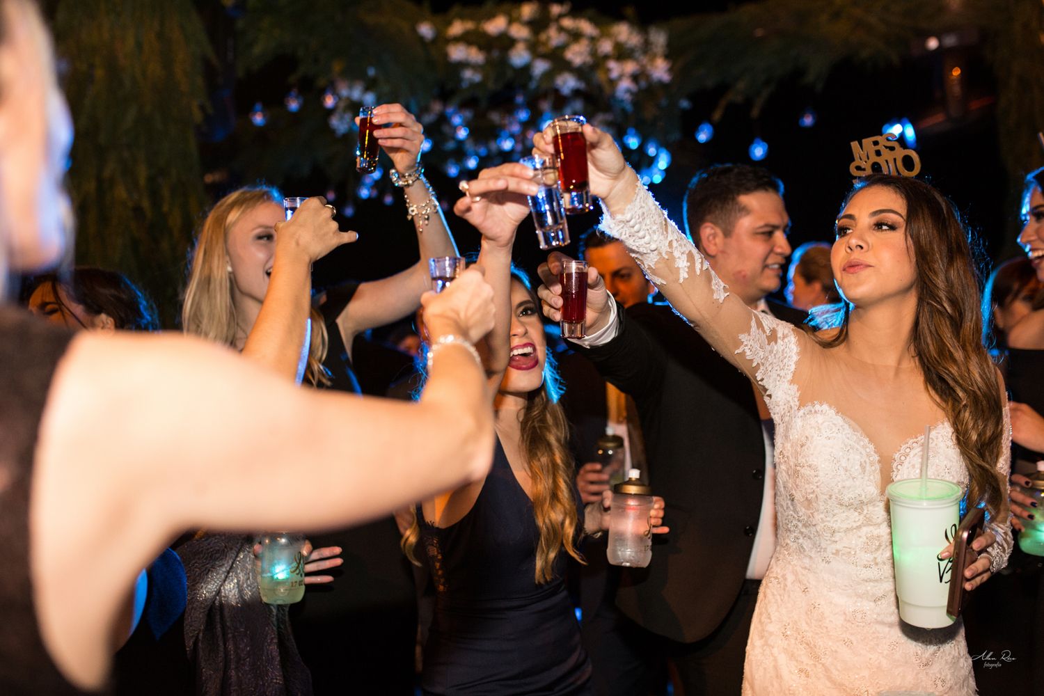 Bride in wedding gown raises drinks with guests during festive wedding reception toast.