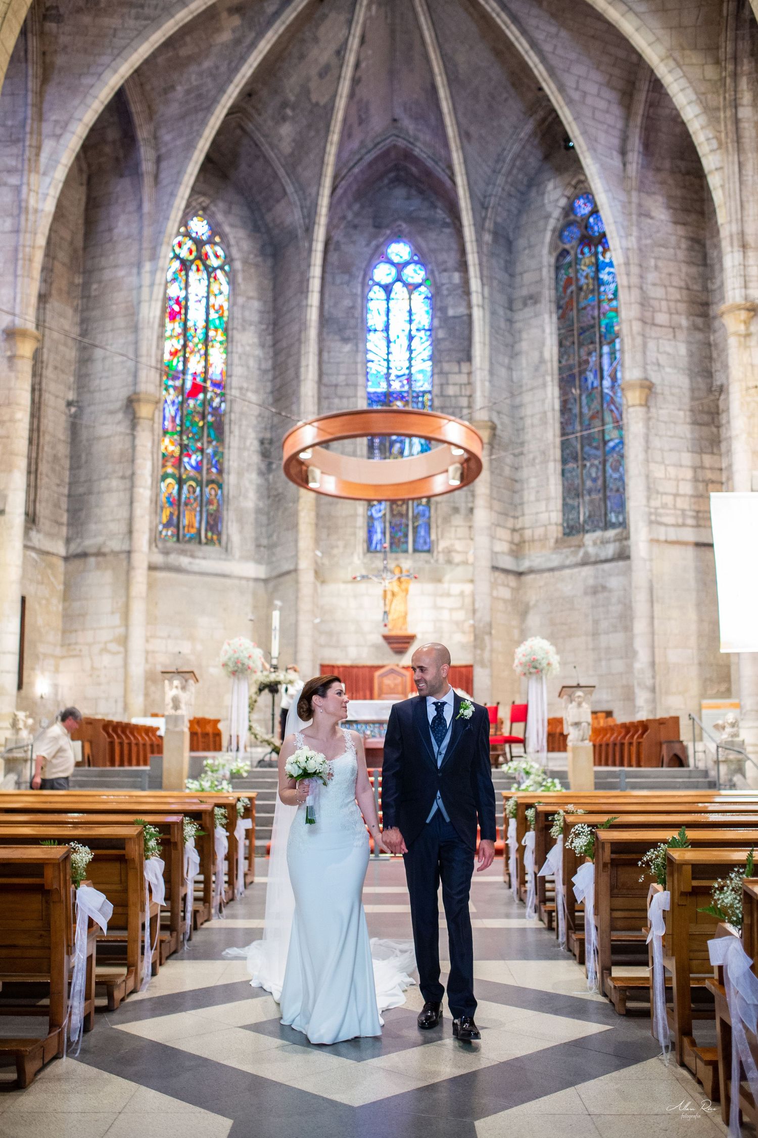 Bride and groom walking hand in hand inside a stunning Gothic church with stained glass windows.