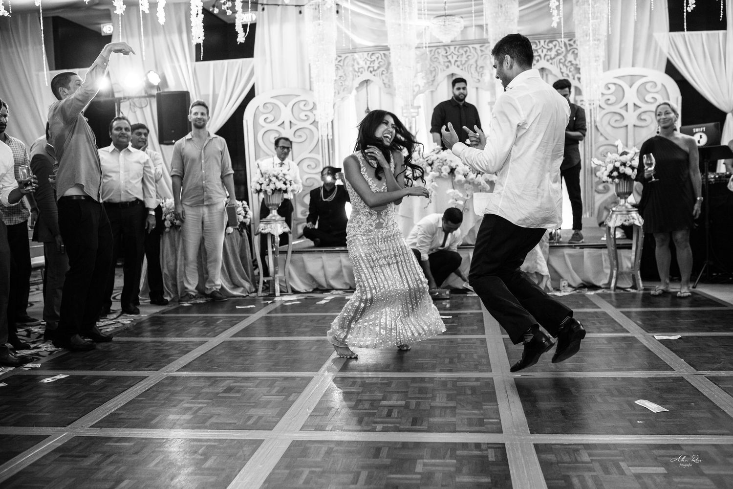 Couple dancing energetically on a ballroom dance floor surrounded by wedding guests in black and white photo.
