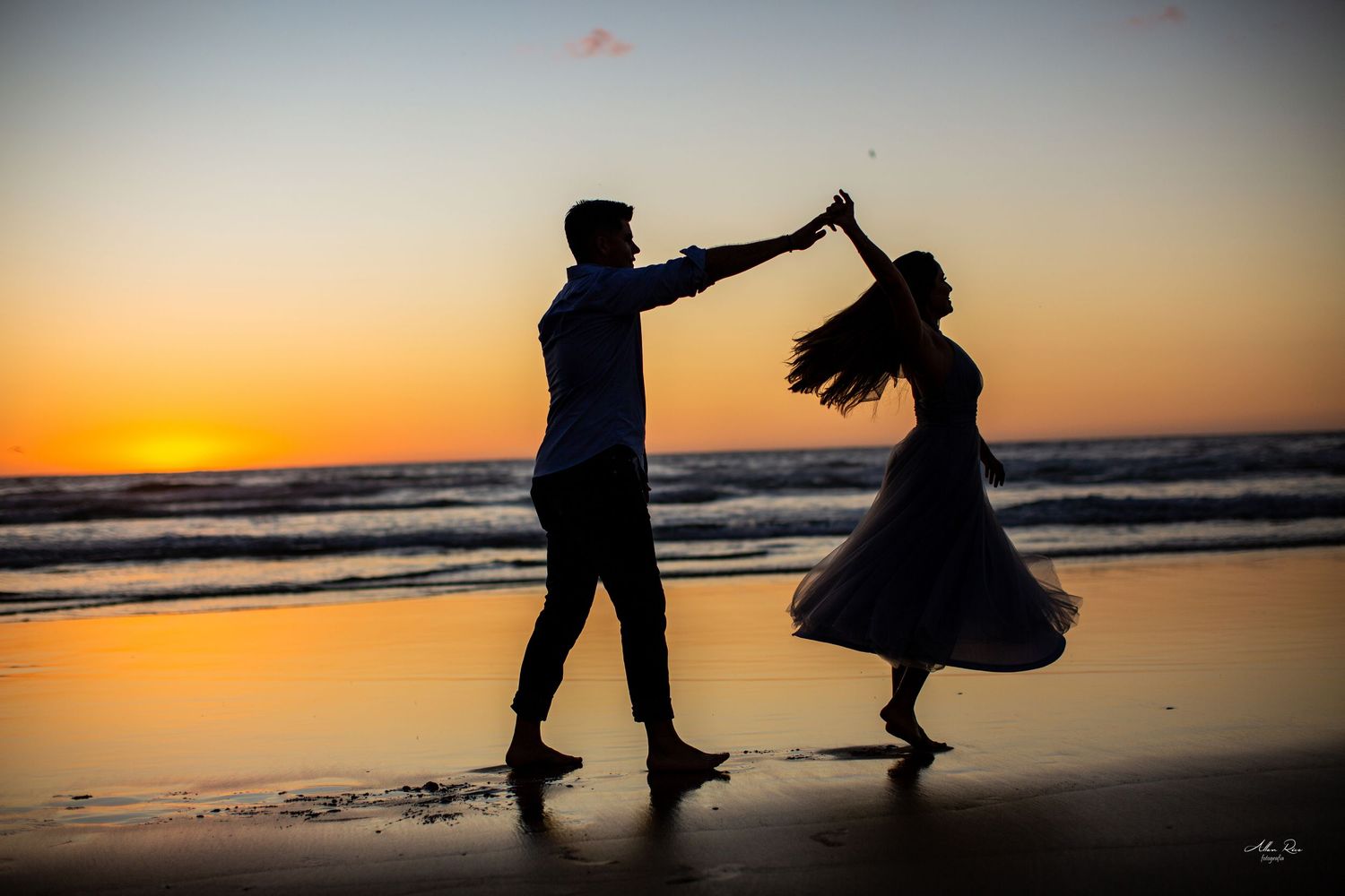 Couple dancing as silhouettes on beach at golden sunset.