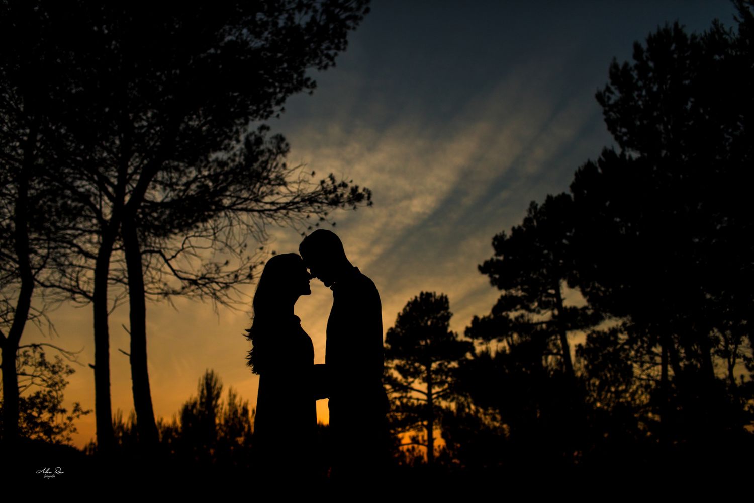 Romantic silhouette of a couple touching foreheads against a stunning colorful sunset sky.
