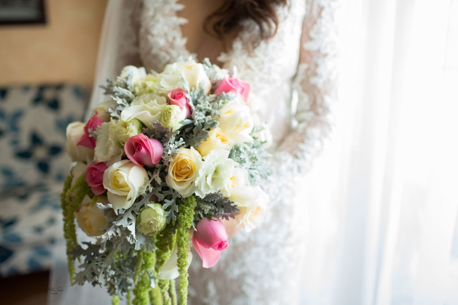 Bride in lace wedding gown holding beautiful bouquet of white and pink roses with greenery.