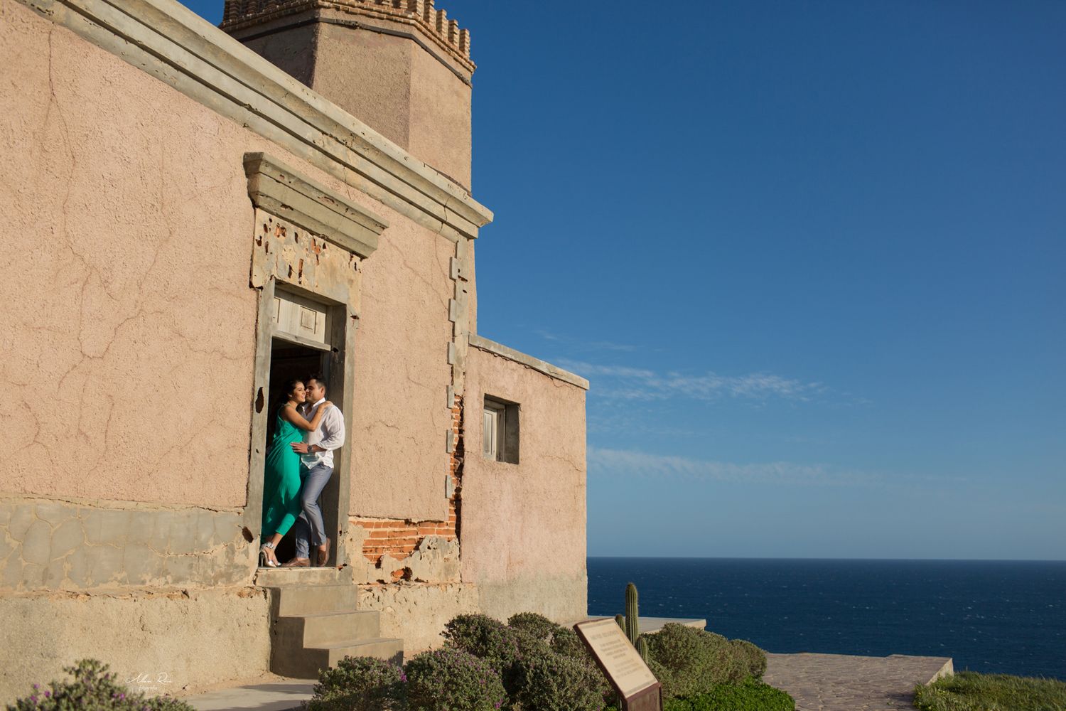 Romantic couple embracing in doorway of historic coastal stone building overlooking the blue ocean.