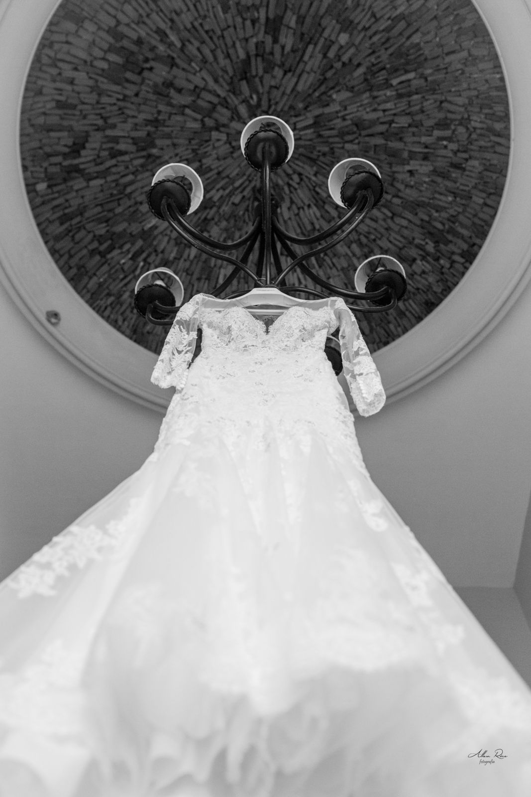 Black and white photo of a lace wedding gown with long sleeves hanging from a decorative chandelier.