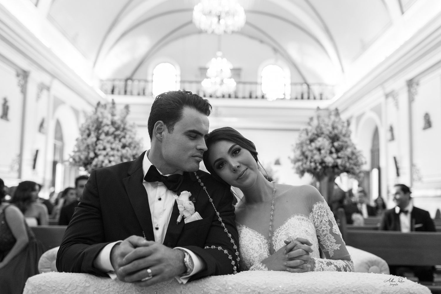 Black and white portrait of bride and groom leaning together in decorated church aisle.