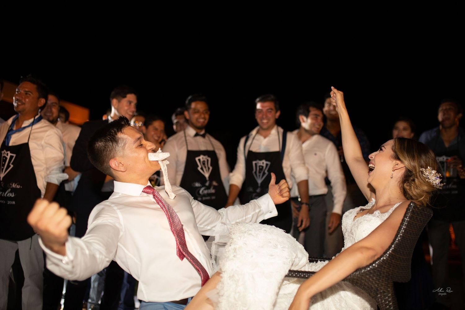 Bride and groom celebrating energetically with cheering wedding party guests at night reception.