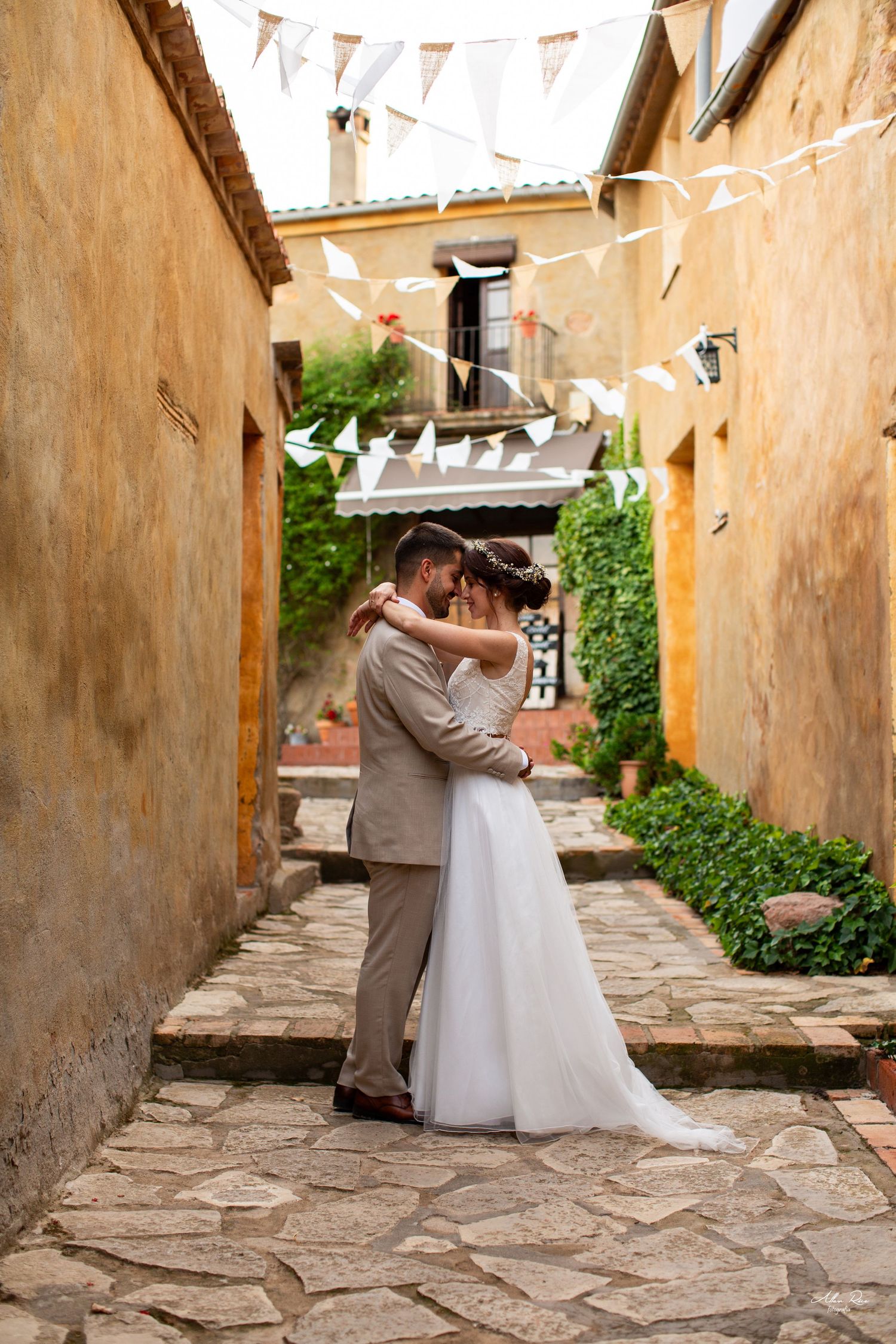 Bride and groom embracing in a charming cobblestone alley decorated with white bunting flags.