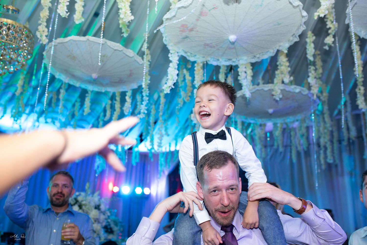 Joyful young boy sitting on a mans shoulders laughing at a beautifully decorated wedding reception venue.