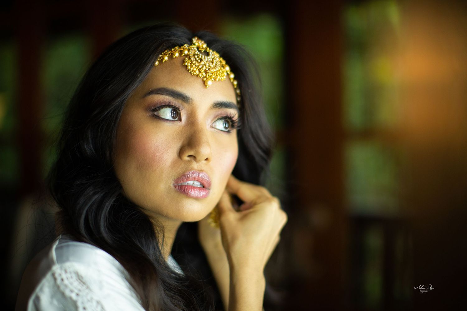 Beautiful Indian bride with gold maang tikka jewelry gazing upward in soft natural light.