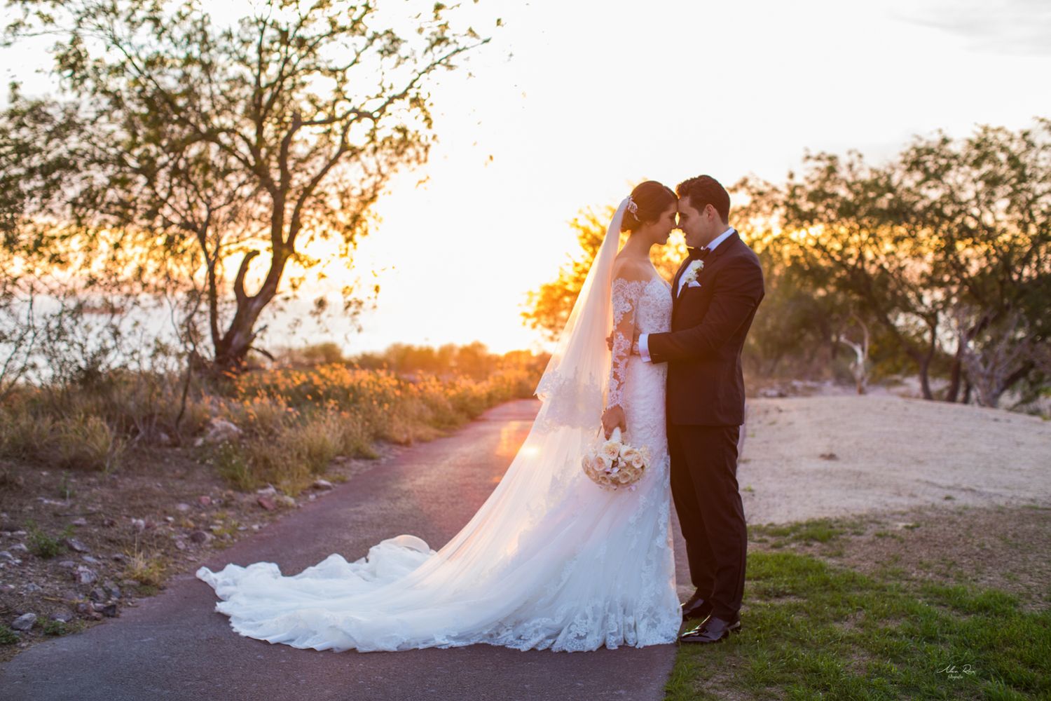 Bride and groom share an intimate moment on a sunlit path at golden hour sunset.
